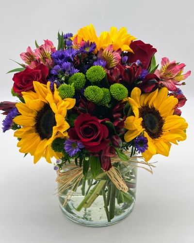 <p>Reminiscent of strolling through a field of flowers, this colorful arrangement captures features magnificent sunflowers, alstroemeria and poms set in a trendy mason jar with a natural raffia bow.</p>