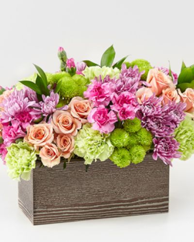 <p>Capture the beauty of the seasons in bloom with our Simple Charm Bouquet. Gorgeous blooms such as peach spray roses, green trick dianthus, pink mini carnations and lavender cushion pompons fill a weathered wooden box with freshness.</p>