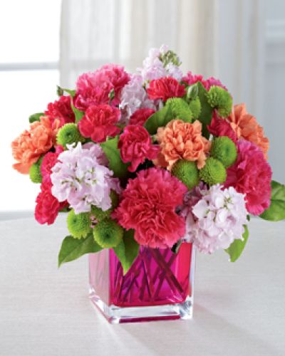 <p>Dazzling and delightful, this bold and colorful flower bouquet is set to impress with it's high impact look and graceful styling. Hot pink carnations, orange carnations, pale pink gilly flower, hot pink mini carnations, green button poms, and lush greens are beautifully arranged in a raspberry pink glass cubed vase to create a rush of fun and warm wishes to send straight to your recipient's door.</p>